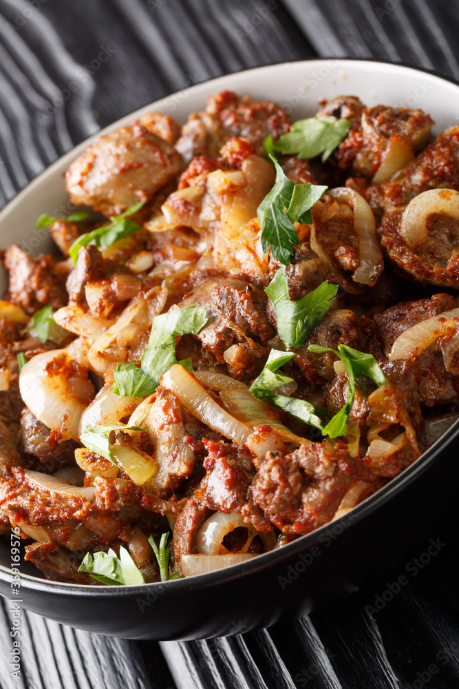 Armenian cuisine fried chicken offal tzhvzhik with onions, tomatoes and spices close-up in a bowl on the table. vertical Armenian cuisine fried chicken offal tzhvzhik with onions, tomatoes and spices close-up in a bowl on the table. vertical