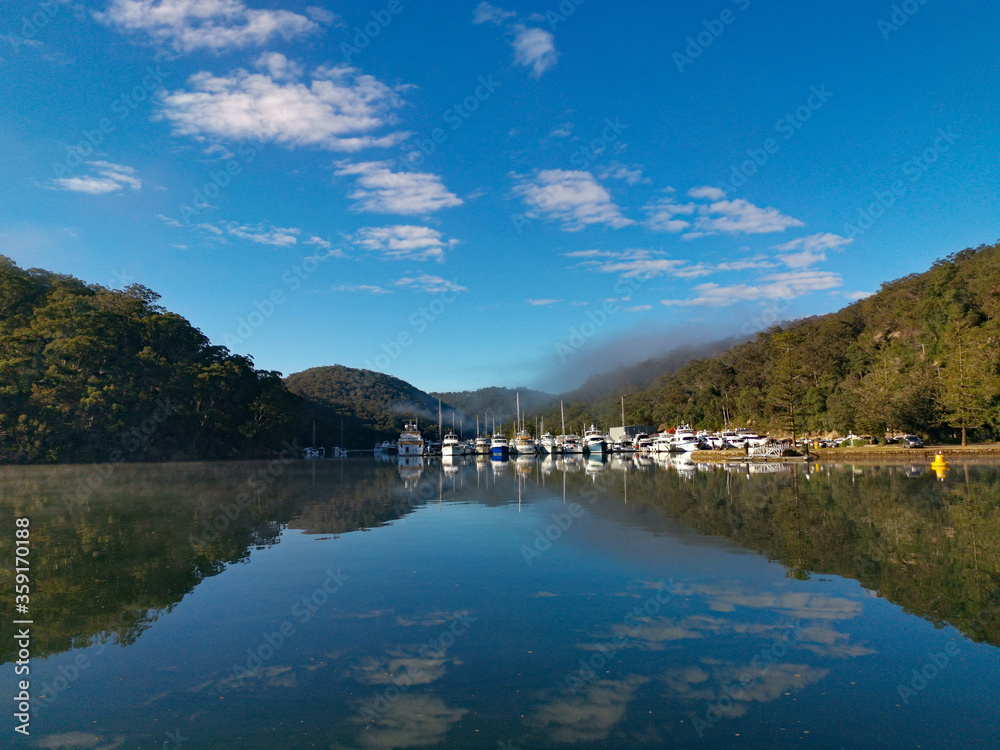 Beautiful morning view of Cowan creek with reflections of blue sky, boats, mountains and trees, Bobbin Head, Ku-ring-gai Chase National Park, New South Wales, Australia