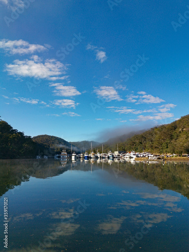 Beautiful morning view of Cowan creek with reflections of blue sky, boats, mountains and trees, Bobbin Head, Ku-ring-gai Chase National Park, New South Wales, Australia © Ivan