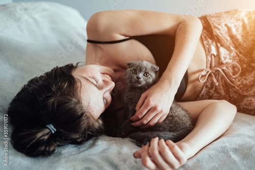 Portrait of Beautiful Young Caucasian White Adult Girl Lying on the Bed with Her Little Cat