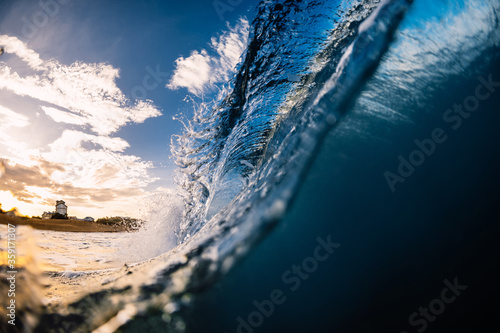 Barrel wave in sea with sunrise tones and beach at background