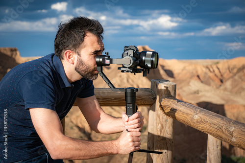 young filmmaker filming natural landscape in canyon with a large river and marshes