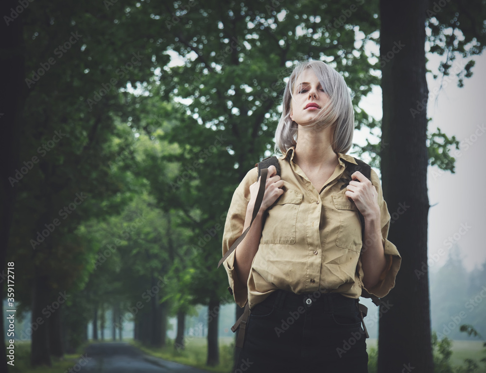 Style blonde woman with backpack at countryside road in rainy day Style blonde woman with backpack at countryside road in rainy day