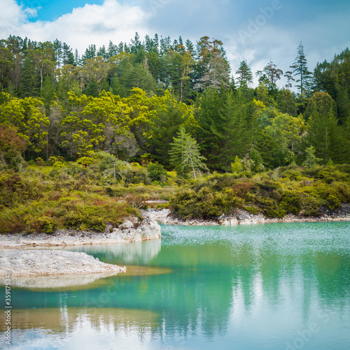 Azure water of geothermal lake refelcts blue sky and surrounding forest photo
