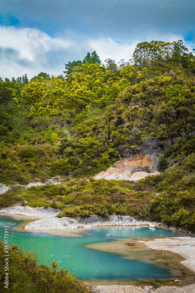 Turquoise waters of geothermal lake surrounded by low trees and shrubbery