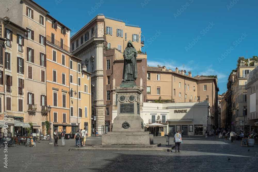 Campo de Fiori in Rome with statue of Giordano Bruno. A few passersby, blue skies.