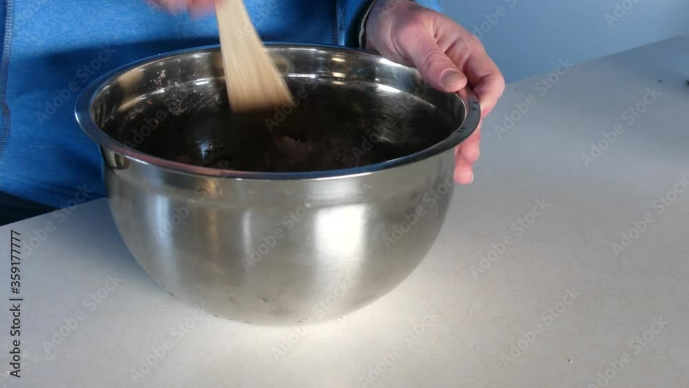 Man walking up to a mixing bowl and beginning mixing with a wooden spoon in a blue jumper Man walking up to a mixing bowl and beginning mixing with a wooden spoon in a blue jumper