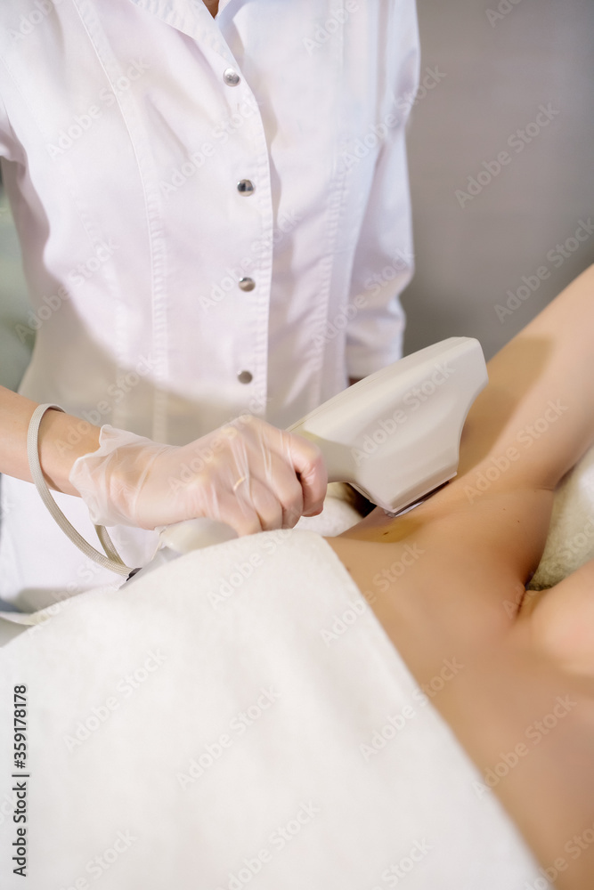 Nurse makes armpit hair removal with a neodymium laser in a medical cosmetology center
