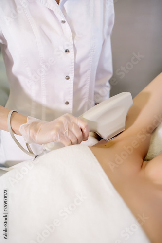 Nurse makes armpit hair removal with a neodymium laser in a medical cosmetology center 