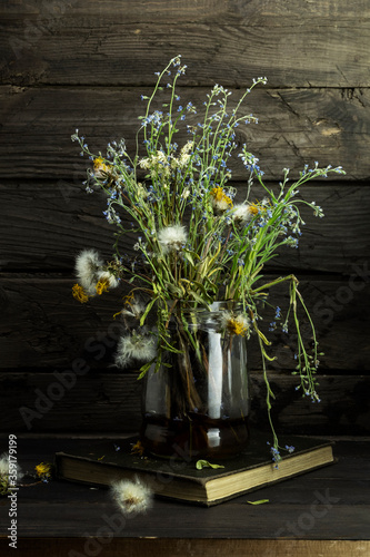 Still life with flowers. Bouquet of wilted flowers in glass jar on wooden table.
