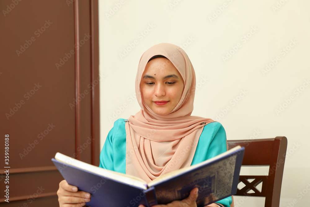 young Asian Malay Muslim woman wearing headscarf at home office student sitting at table read book document note study smile happy look young Asian Malay Muslim woman wearing headscarf at home office student sitting at table read book document note study smile happy look