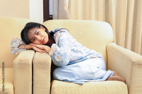 young Asian Malay Muslim woman wearing baju kurung dress at home sit rest on sofa