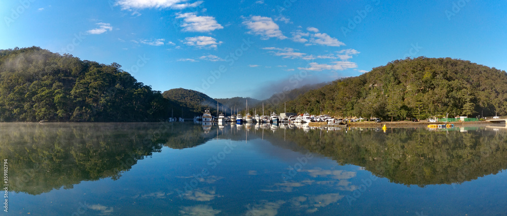 Obraz premium Beautiful morning panoramic view of Cowan creek with reflections of blue sky, boats, mountains and trees, Bobbin Head, Ku-ring-gai Chase National Park, New South Wales, Australia