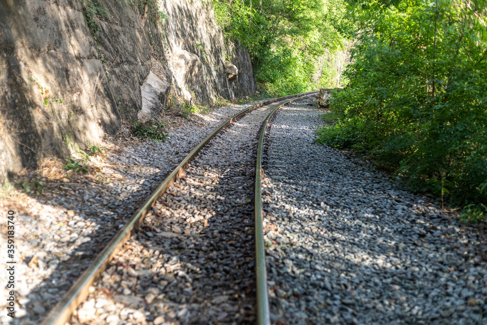 Obraz premium Landscape and midground focus shot of railway under shade of forest trees. Trekking trail along railway covered with forest shadow