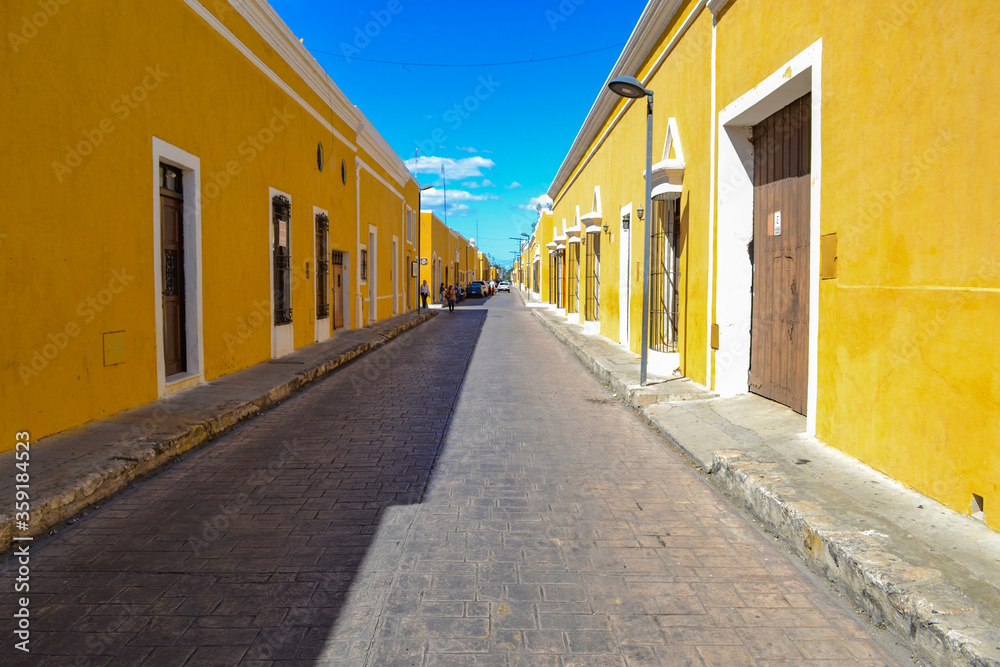 Street view of colonial architecture yellow houses on a cityscape in medieval Unesco world heritage Izamal on the Yucatan Peninsula in Mexico with wooden doors, white frames and rustic painted walls