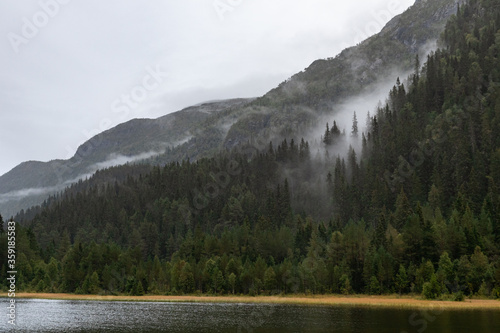 Clouds on lake in Norway mountains. Autumn travel wild nature. Foggy scandinavia cloudy pine forest