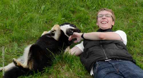 Fotografie Young happy man plays with dog (Lapland Reindeer dog) in summer on grass