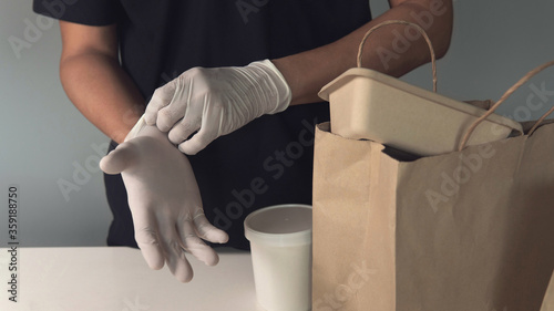 Man’s hand putting white latex or rubber gloves on for checking and ready to delivery environmentally friendly recyclable paper food packaging. Healthcare concept and supporting small businesses