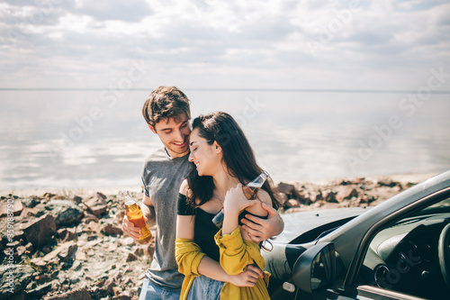 Travel, tourism - Man and woman drink champagne near the water at a folding portable table. Picnic near the water. Couple going on Adventure. Car travel concept.
