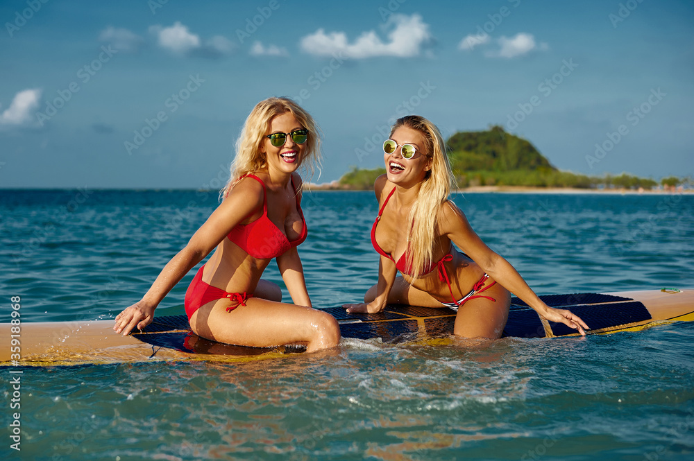 Beautiful women having fun on surfboard in the sea. Outdoor fashion summer portrait
