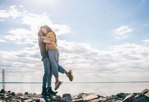 Love and travel. A couple stands against the backdrop of the bay. A man and a woman are standing near a river or sea on stones and hugging.