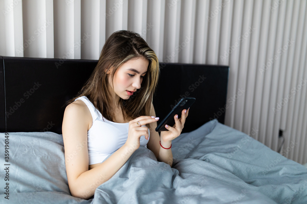 Young woman holds her phone in front of her as she looks forward while on the bed.