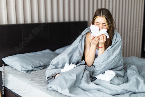 Young pretty woman sneezing nose covered by warm duvet photo