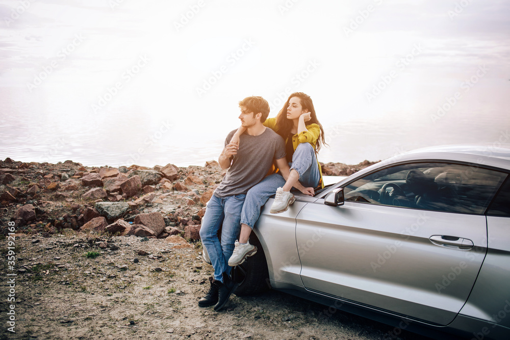 young couple by a sports car parked on the beach. Romance and love in a car trip