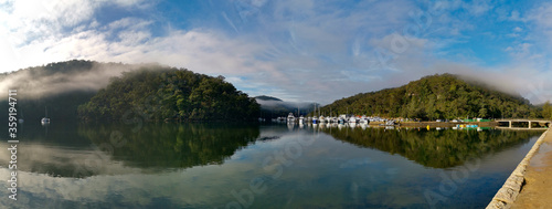 Beautiful morning panoramic view of Cockle creek with reflections of blue sky  light clouds  foggy mountains and trees  Bobbin Head  Ku-ring-gai Chase National Park  New South Wales  Australia