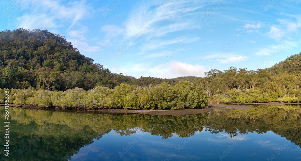 Beautiful morning view of Cockle creek with reflections of blue sky, foggy mountains and trees, Bobbin Head, Ku-ring-gai Chase National Park, New South Wales, Australia