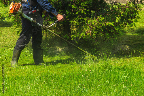A man mows the grass with a gasoline scythe