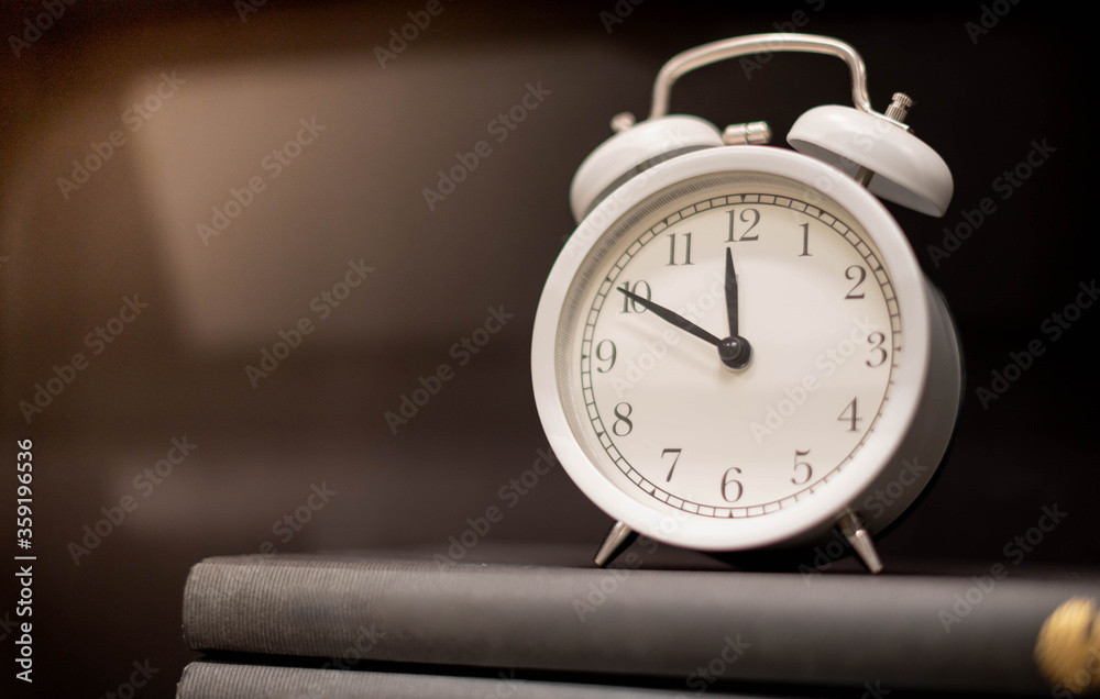 Classic white clock on the pile of books on the wooden backdrop for show the timing of life and time is important concept. Classic white clock on the pile of books on the wooden backdrop for show the timing of life and time is important concept.