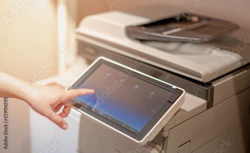 Female hand pressing the touchscreen monitor of the copy machine for copy a paper document,