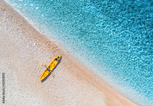 Aerial view of empty sandy beach with yellow canoe, sea coast with transparent blue water in sunny bright day in summer. Travel in Croatia. Top view of boat. Landscape with kayak at sunset. Travel