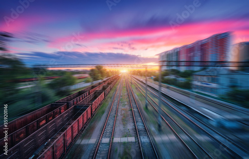 Aerial view of railroad and colorful sky with clouds at sunset with motion blur effect in summer. Industrial landscape with freight train, railway station, blurred background.  Railway platform © den-belitsky