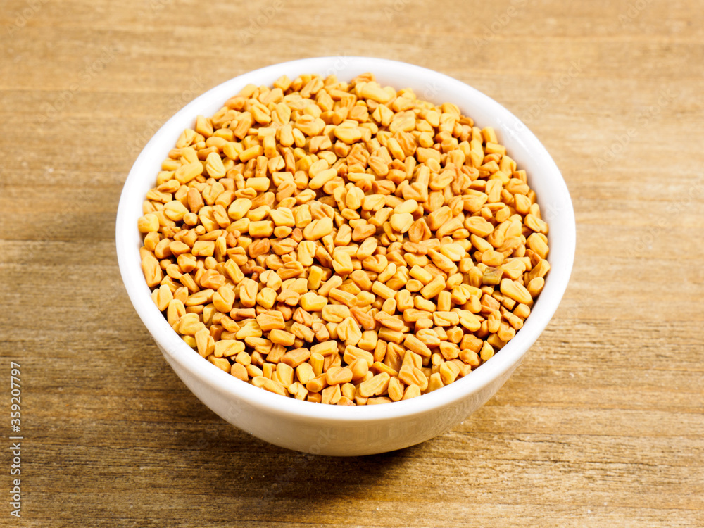 Spice fenugreek in white bowl on brown wood background with copy space Spice fenugreek in white bowl on brown wood background with copy space