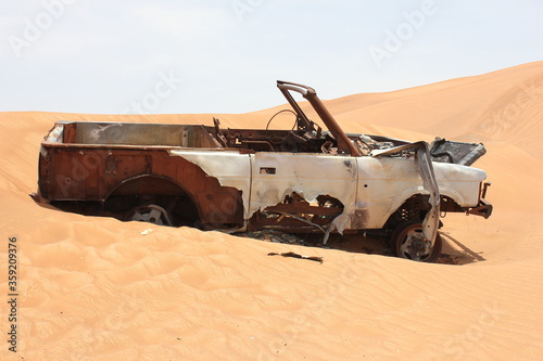 Burnt out wreckage of a SUV (4-wheel-drive) vehicle rusts away in hot and arid desert sand dunes terrain in Sharjah emirate in the United Arab Emirates.  