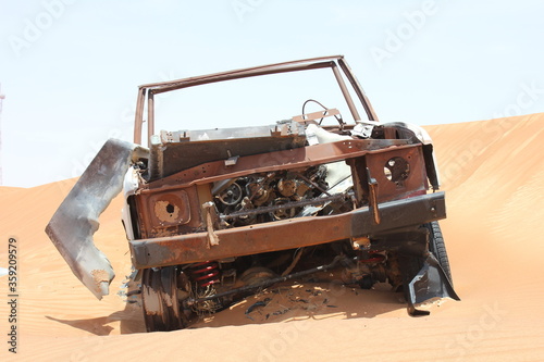 Burnt out wreckage of a SUV (4-wheel-drive) vehicle rusts away in hot and arid desert sand dunes terrain in Sharjah emirate in the United Arab Emirates.  