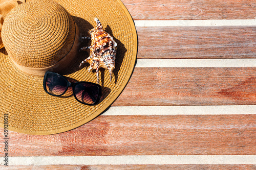 Top view of a female straw hat on a wooden background with seashells and slippers. The concept of vacation and sea vacation photo