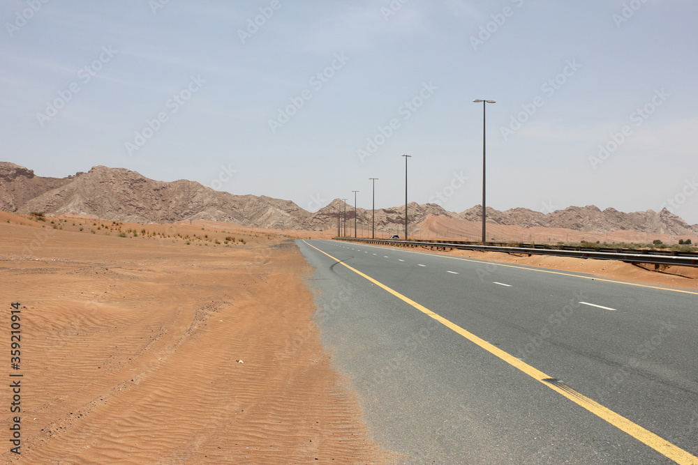 Modern asphalt highway passes through arid desert sand dunes terrain in Sharjah emirate in the United Arab Emirates.  