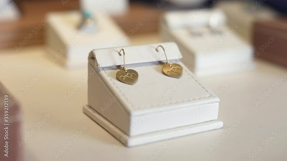 Close up video of golden earrings. A Heart Shaped Golden Earrings With Mountain Engravings Displayed At A Jewelry Shop. Close up video of golden earrings. A Heart Shaped Golden Earrings With Mountain Engravings Displayed At A Jewelry Shop.