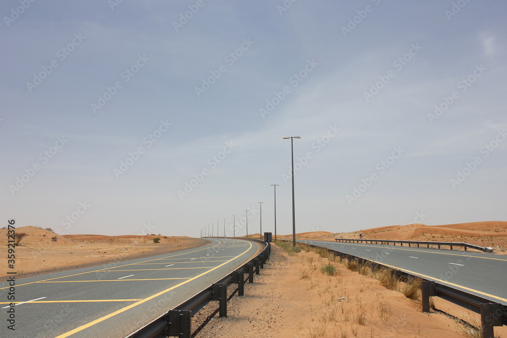 Modern asphalt highway passes through arid desert sand dunes terrain in Sharjah emirate in the United Arab Emirates.  