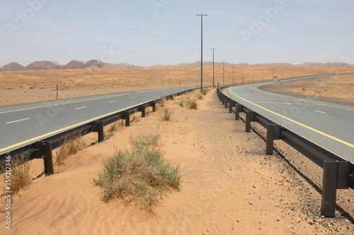 Modern asphalt highway passes through arid desert sand dunes terrain in Sharjah emirate in the United Arab Emirates.  