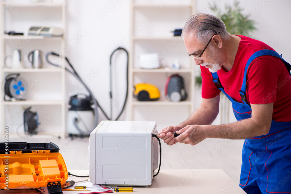 Old male contractor repairing microwave indoors Old male contractor repairing microwave indoors