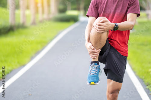 Young adult male in red sportswear stretching muscle in the park outdoor, runner man warm up ready for running and jogging in morning. wellness, fitness, exercise and healthy lifestyle concepts