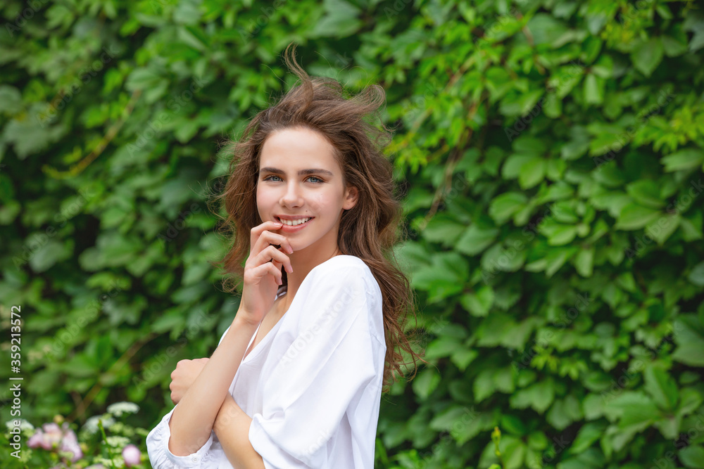 Beautiful and cute young girl in the summer in the Park against a green wall with plants Beautiful and cute young girl in the summer in the Park against a green wall with plants