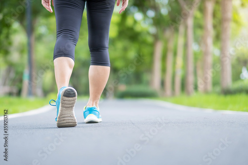 Young adult female in sport shoes running in the park outdoor, woman jogging and walking on the road at morning, leg muscles of Athlete. Exercise, wellness, healthy lifestyle and workout concepts