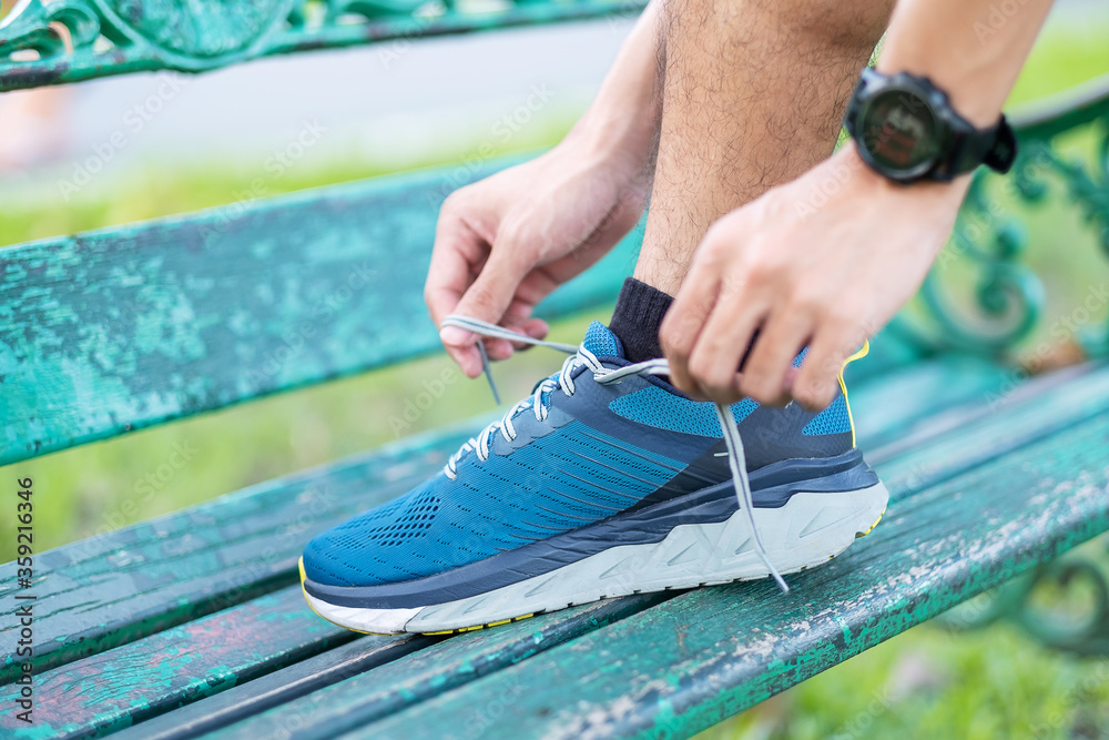 Fototapeta premium Young adult male in sportswear and smartwatch tying shoelace in the park outdoor, athlete runner man ready for running and jogging in morning. Exercise, wellness, healthy lifestyle and workout concept