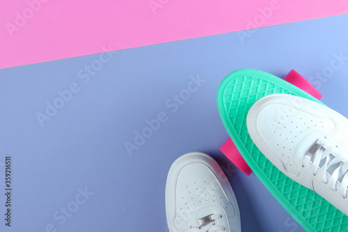 White sneakers on plastic mini cruiser board. Pastel color background. Top view