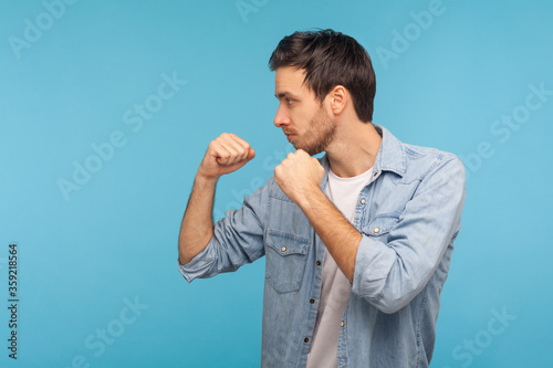 Canvas Print Side view of man in worker denim shirt standing with boxing gesture, punching to camera, provoking fight or ready to self-defense, struggle concept